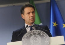 Il Presidente del Consiglio Giuseppe Conte parla, sullo sfondo bandiere Italia e UE