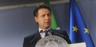 Il Presidente del Consiglio Giuseppe Conte parla, sullo sfondo bandiere Italia e UE
