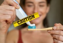 Allarme dentifrici, occhio a quelli per i bambini: contengono qualcosa di spaventoso! donna che mette dentifricio su spazzolino e scritta gialla caution