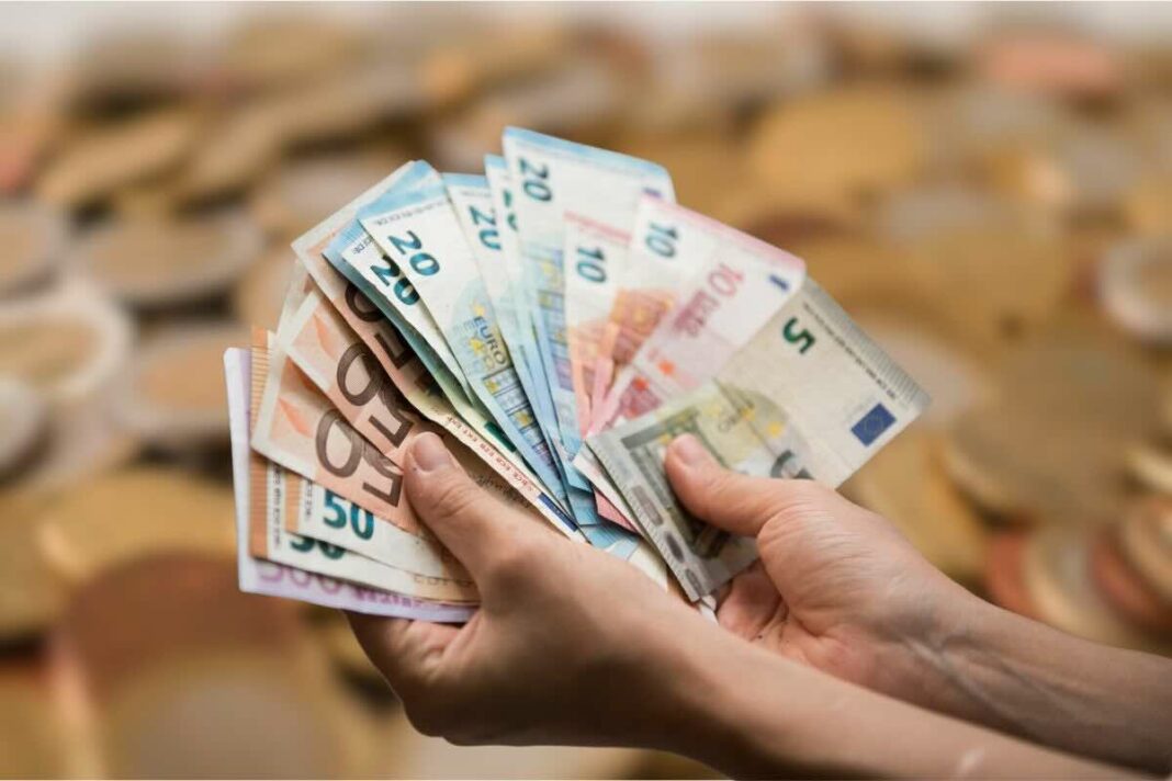 mani di persona con banconote in euro e sfondo di monete