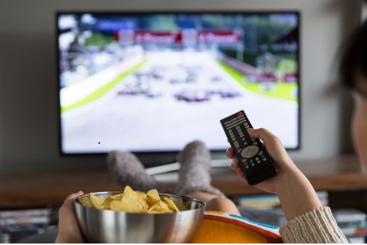mano con telecomando e patatine di persona che guarda la tv
