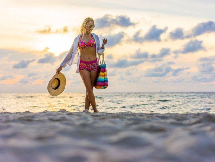 donna in costume che cammina sulla spiaggia al tramonto