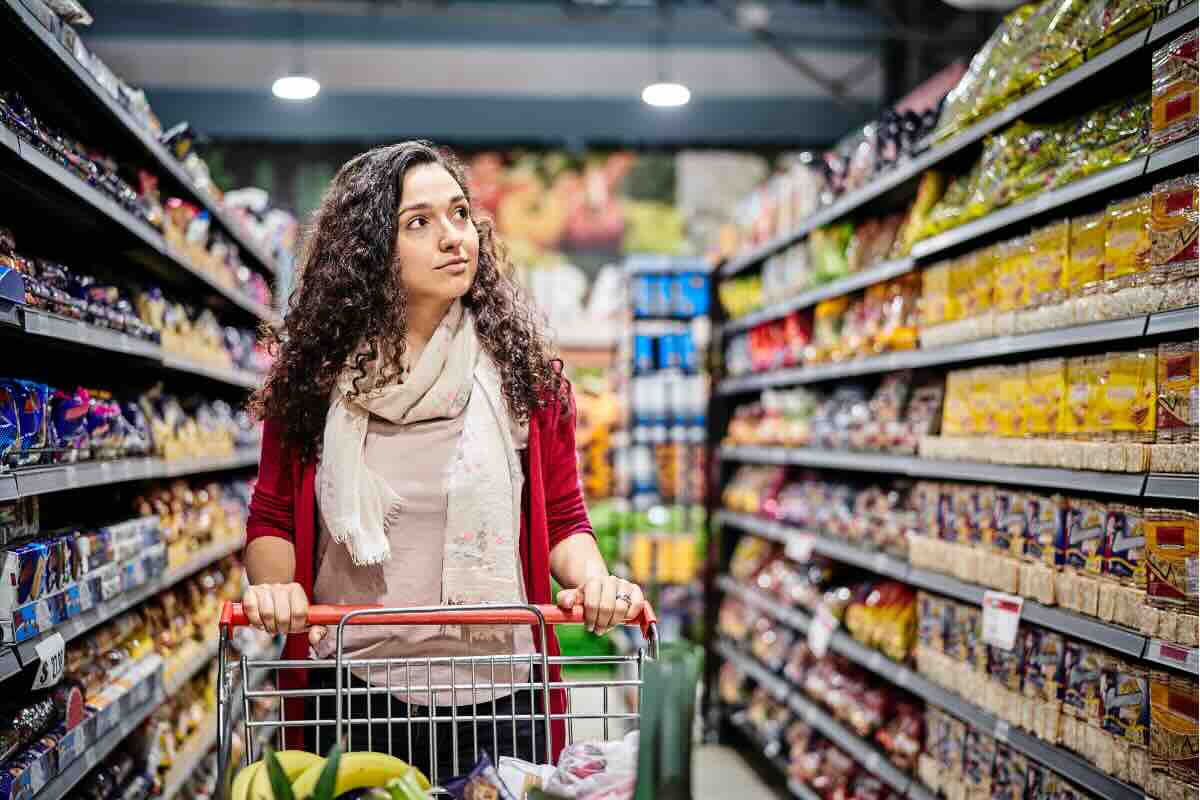 donna con carrello tra gli scaffali del supermercato