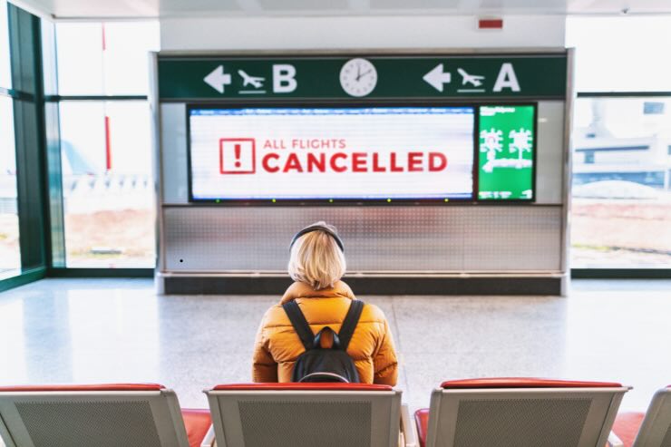 donna seduta all'aeroporto e scritta del volo cancellato