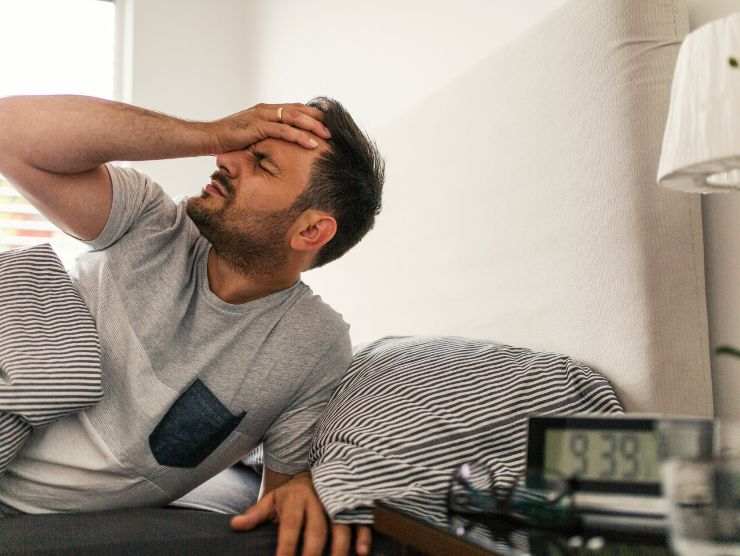 uomo che si alza dal letto con mal di testa