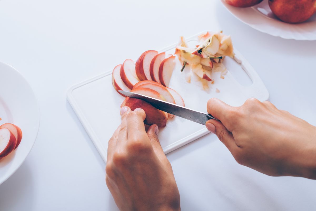 persona che sta affettando una mela su un tagliere di plastica
