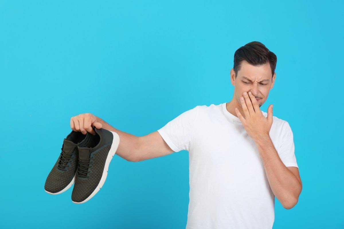 uomo che mantiene scarpe che puzzano