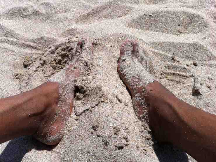 piedi in spiaggia pieni di sabbia