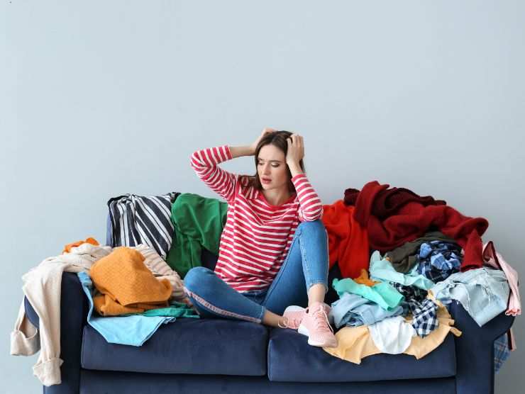 donna seduta su in divano pieno di vestiti