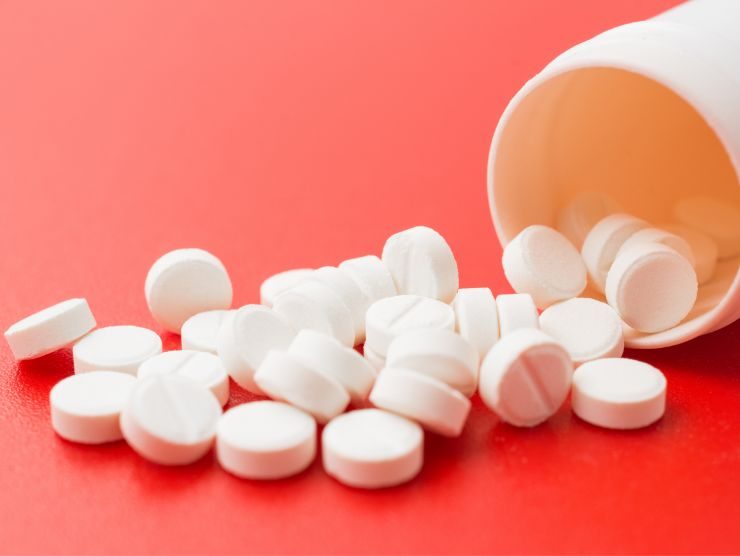 flacone di pillole bianche versate su una superficie rossa