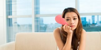 donna che piange sul divano con una metà di cuore di carta in mano