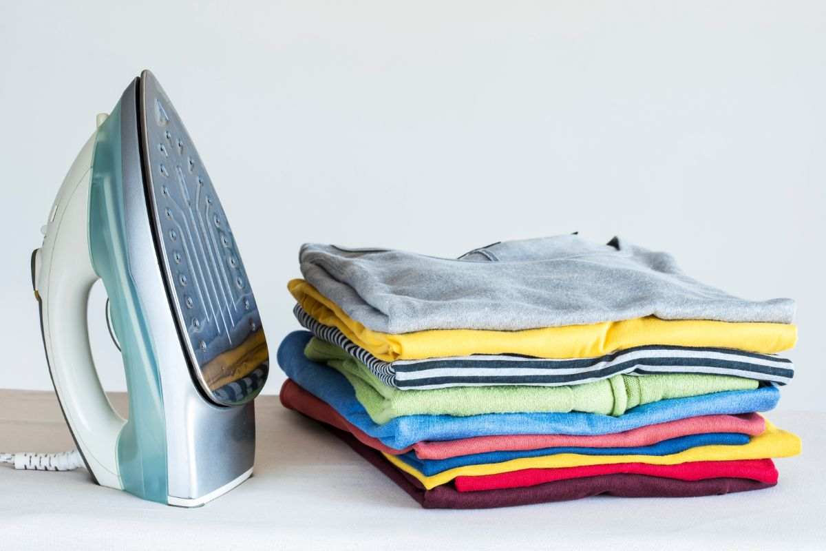 ferro da stiro e pila di magliette piegate e stirate