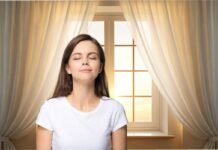 donna che sente profumo nell'aria e alle sue spalle una finestra con tende