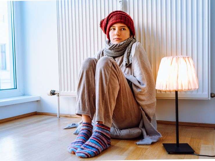 donna seduta a terra vicino ad un termosifone che sente freddo