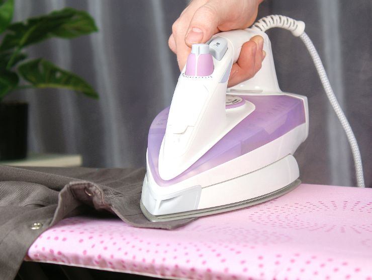 mano che impugna ferro da stiro e lo passa su una camicia