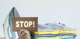 mano che mantiene un cartello con scritta stop e ferro da stiro con capi appena stirati