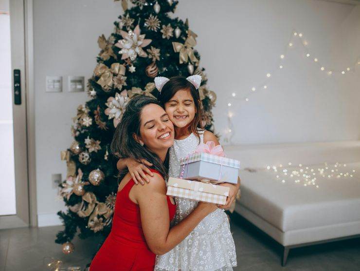 mamma e figlia che si scambiano un regalo davanti ad un albero di natale