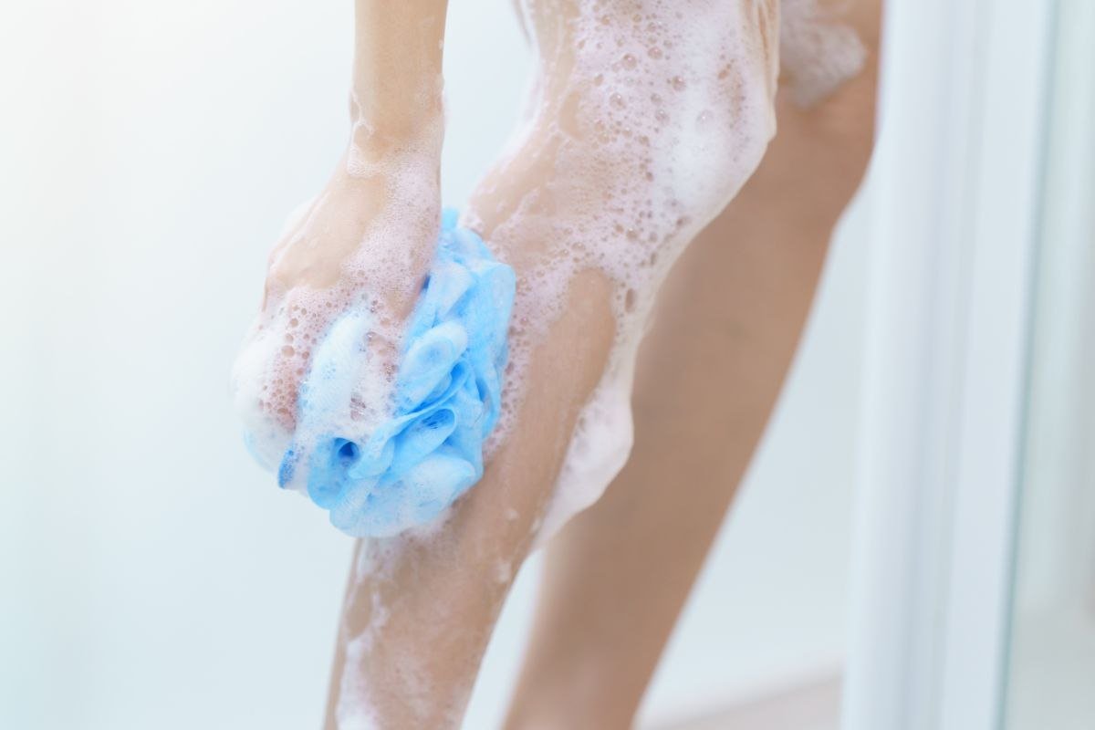 persona sotto la doccia che s'insapona le gambe